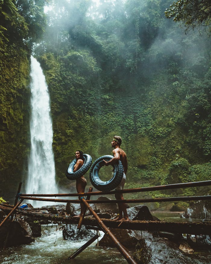 A couple in swimwear with float tubes exploring a lush waterfall in Bali, Indonesia.