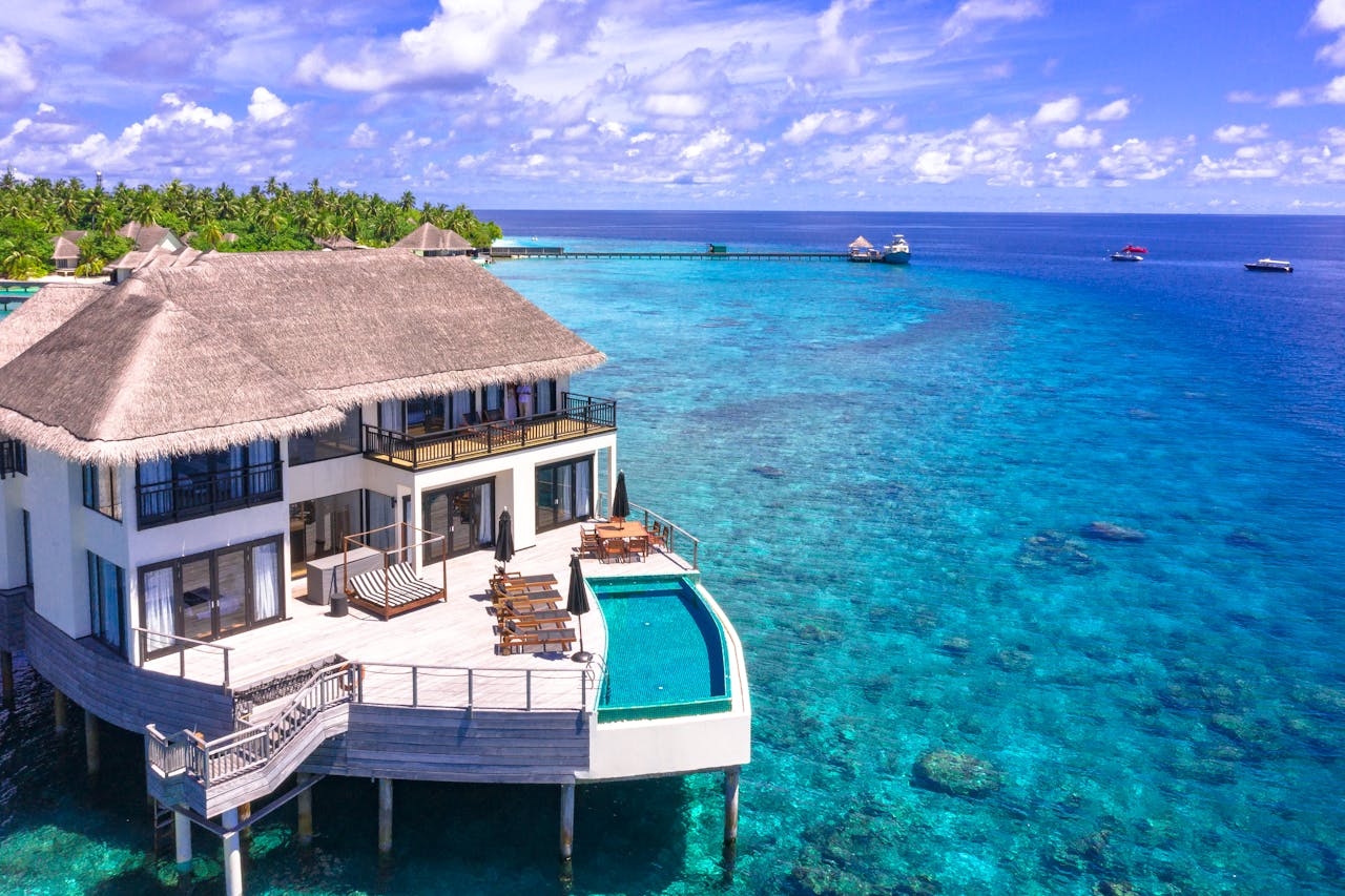 Aerial view of a luxurious overwater villa with infinity pool in a tropical resort, surrounded by clear blue ocean.